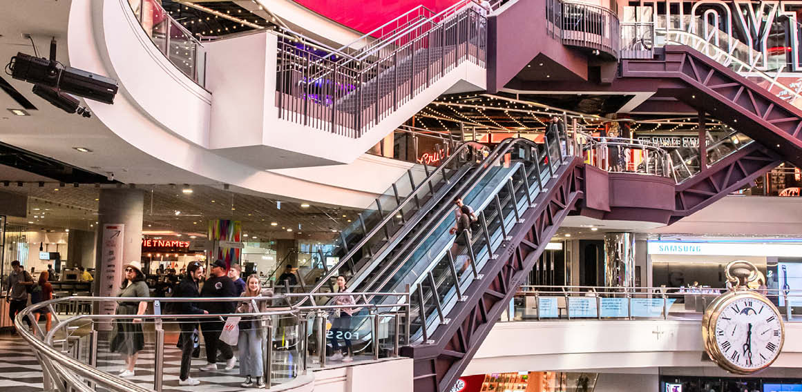 Centro comercial con escaleras mecánicas, tiendas y pantallas