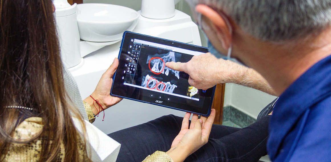 Profesional y cliente revisan radiografía a través de dispositivo electrónico propiedad de la clínica dental