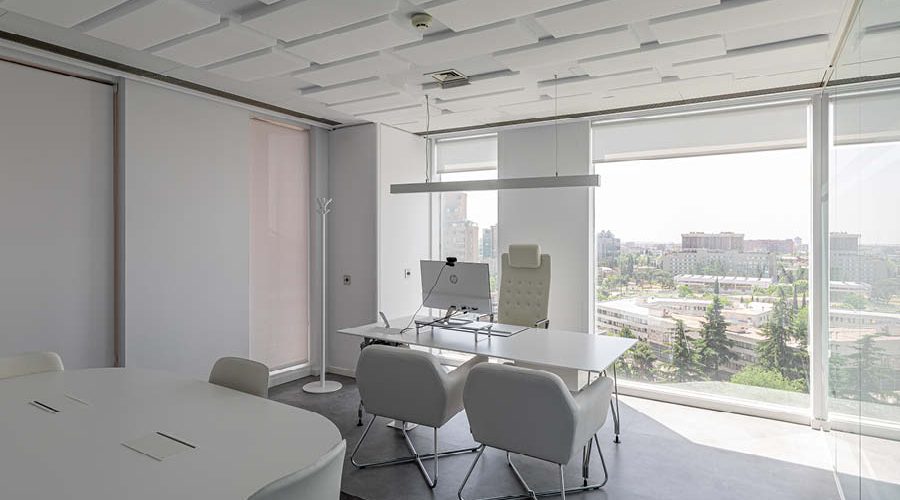 Despacho individual con mobiliario en tonos blancos, butacas y gran ventanal con iluminación natural