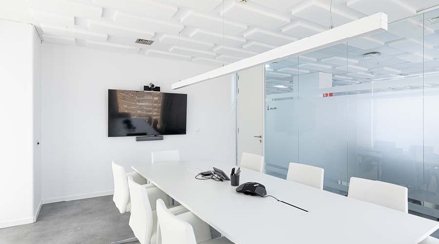 Sala de reuniones y videoconferencias con pantalla, video, mesa grande y sillas, cerramiento con mampara