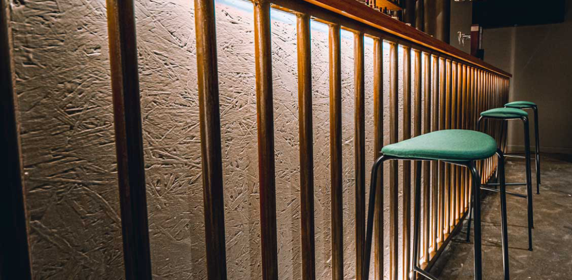 Barra de bar a medida iluminada y con tabretes y mobiliario
