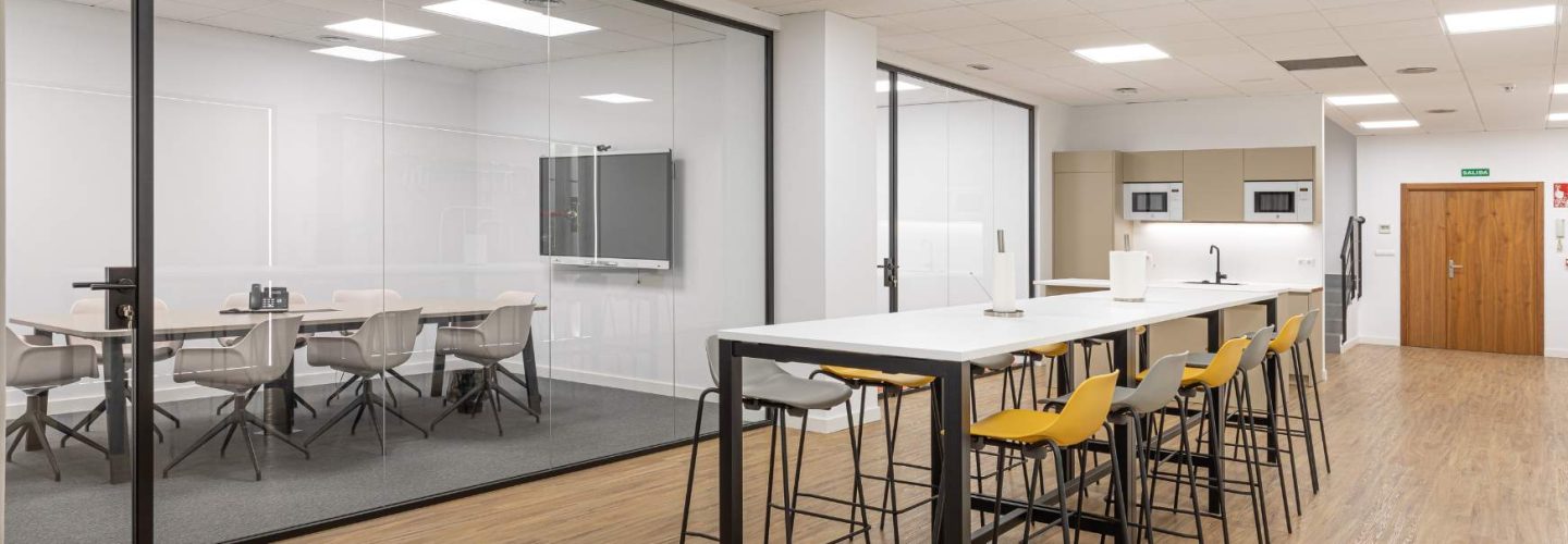 Zona de office con mesa compartida y sala de reuniones compartimentada en oficina