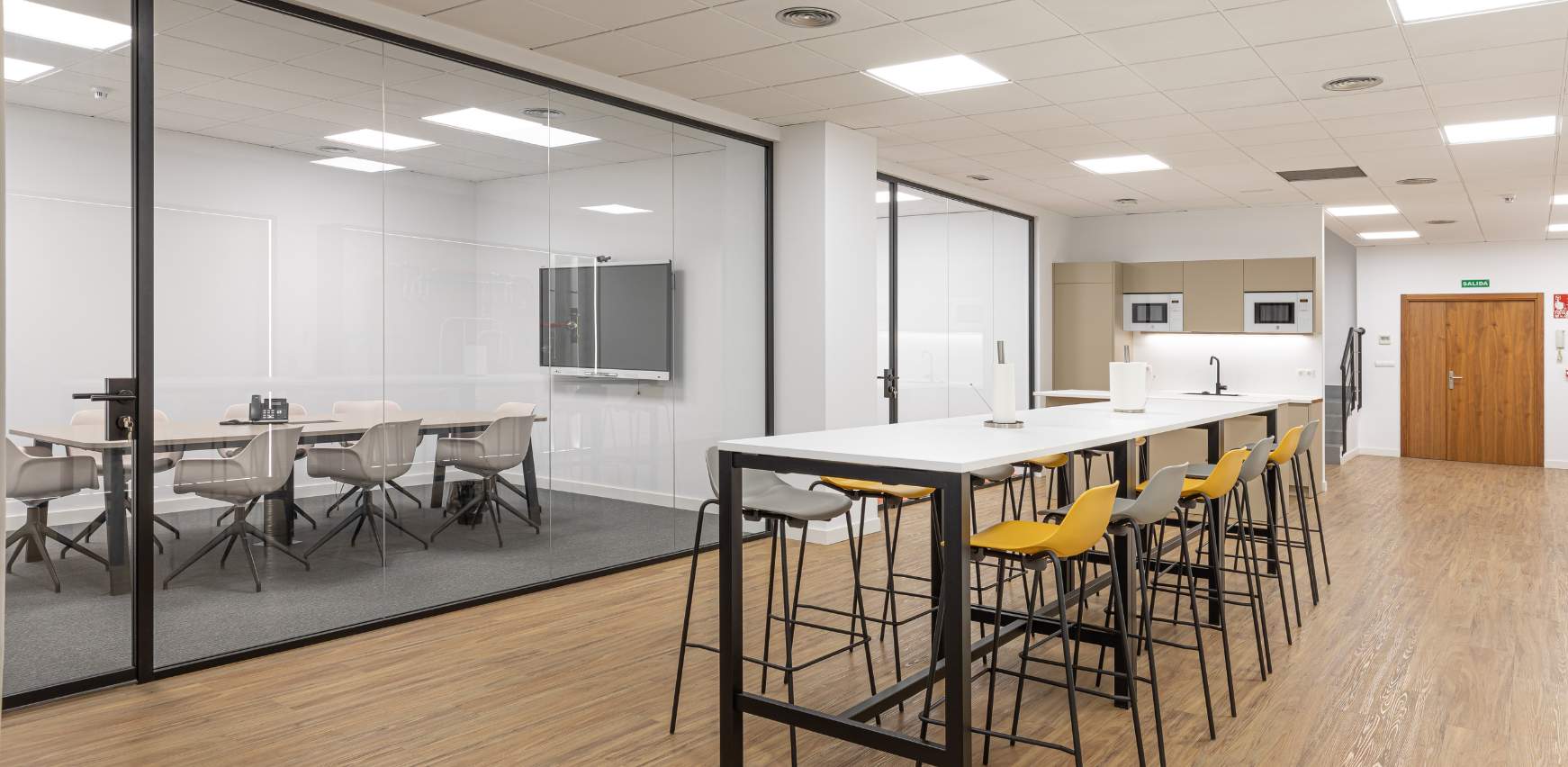 Zona de office con mesa compartida y sala de reuniones compartimentada en oficina