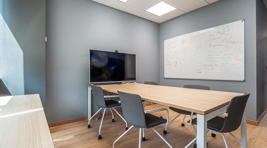 Sala de reuniones con pantalla, sillas y mesa en oficina funcional