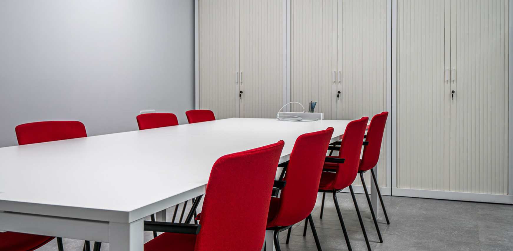 Sala de reuniones con mesa, armarios de almacenaje y sillas en oficina moderna
